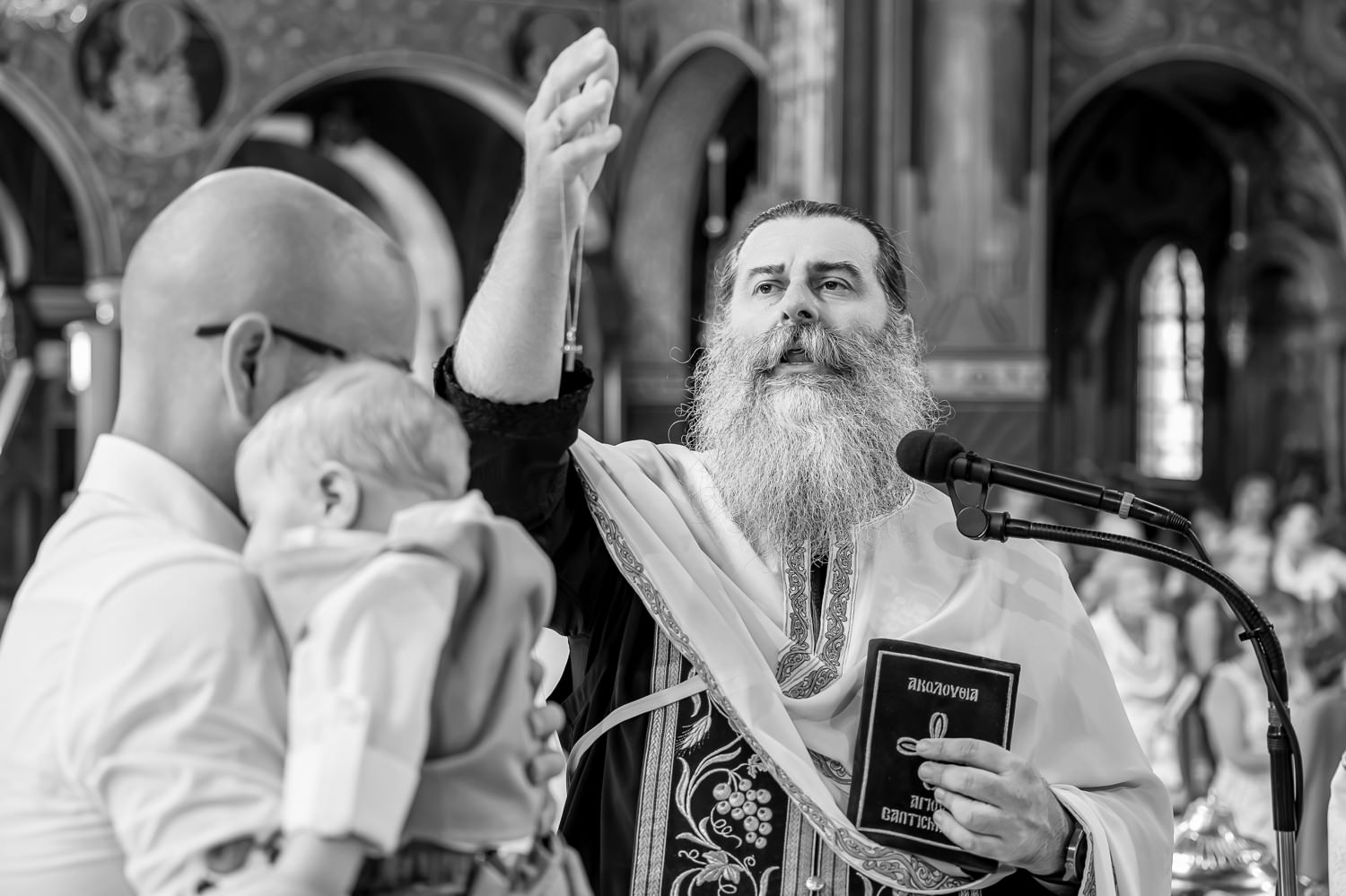 Φωτογράφηση βάπτισης διδύμων στη Λάρισα. Ασπρόμαυρη φωτογραφία ιερέα που ευλογεί κατά τη διάρκεια της τελετής.